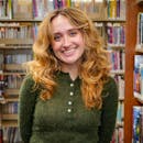Cheerful young woman smiling while standing in a vibrant library setting.